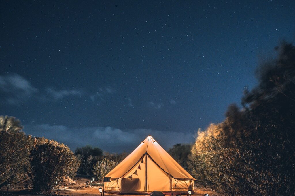 Tente de glamping éclairée sous un ciel étoilé, entourée de nature sauvage en Provence-Alpes-Côte d’Azur, offrant une expérience immersive en plein air.